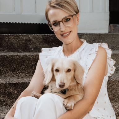 Junge Frau mit einem goldenen Dackeln auf dem Schoß sitzt auf einer Treppe.